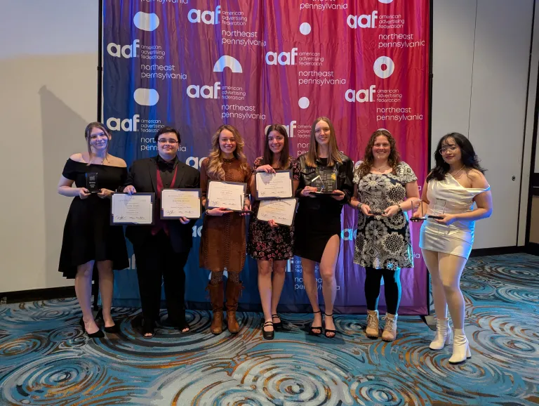 A group of art students standing in front of a backdrop with the AAF logo, holding their awards for their creative work.